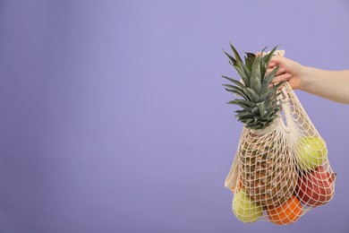 Photo of Woman with string bag of fresh fruits on violet background, closeup. Space for text