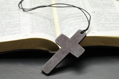 Photo of Wooden Christian cross and Bible on black table, closeup