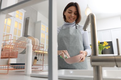 Photo of Happy young woman washing plate above sink in modern kitchen