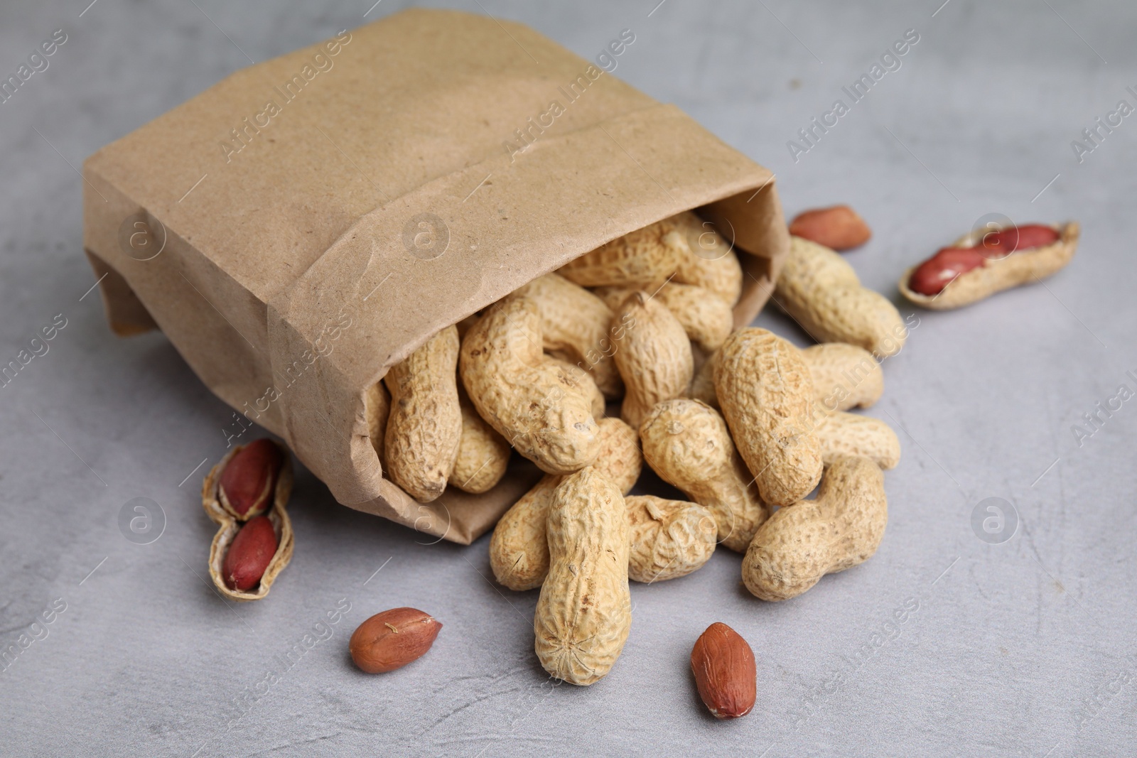 Photo of Paper bag with fresh unpeeled peanuts on grey table, closeup