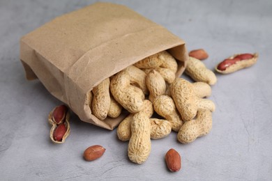 Photo of Paper bag with fresh unpeeled peanuts on grey table, closeup