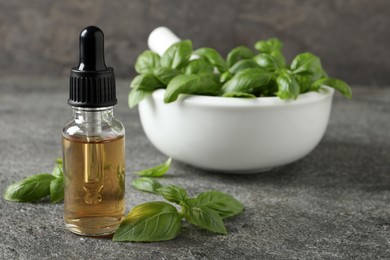 Photo of Glass bottle of basil essential oil and leaves on grey stone table, space for text