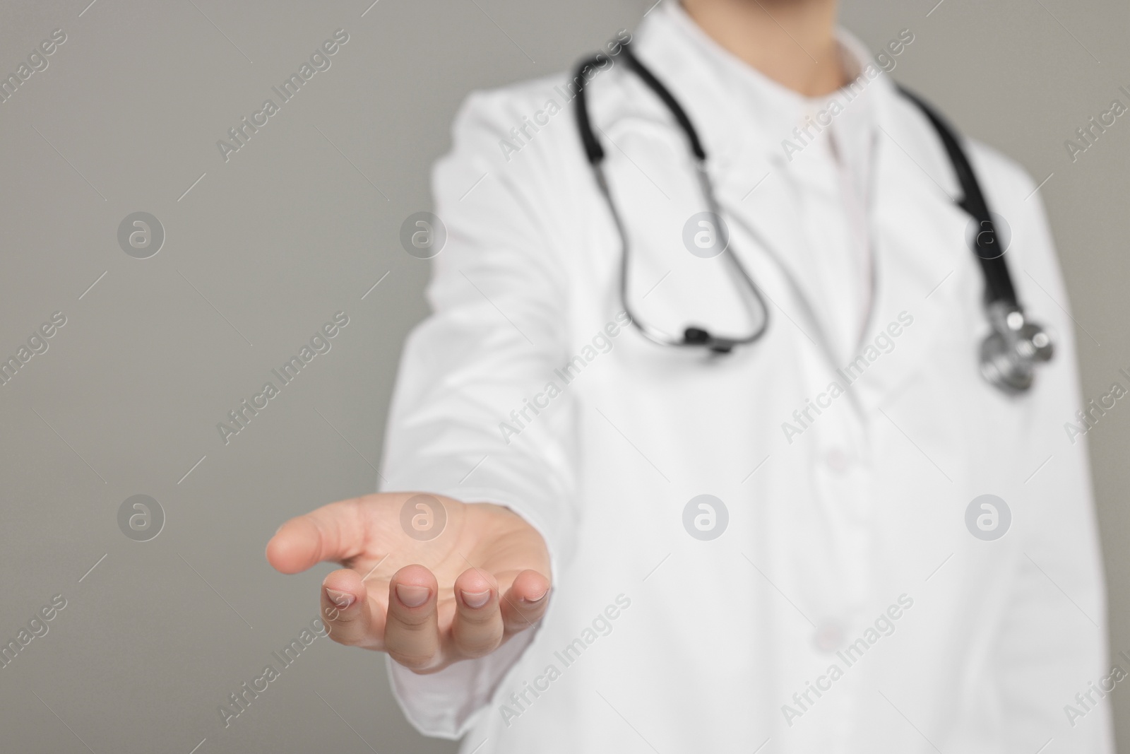 Photo of Doctor with stethoscope holding something on grey background, closeup. Space for text