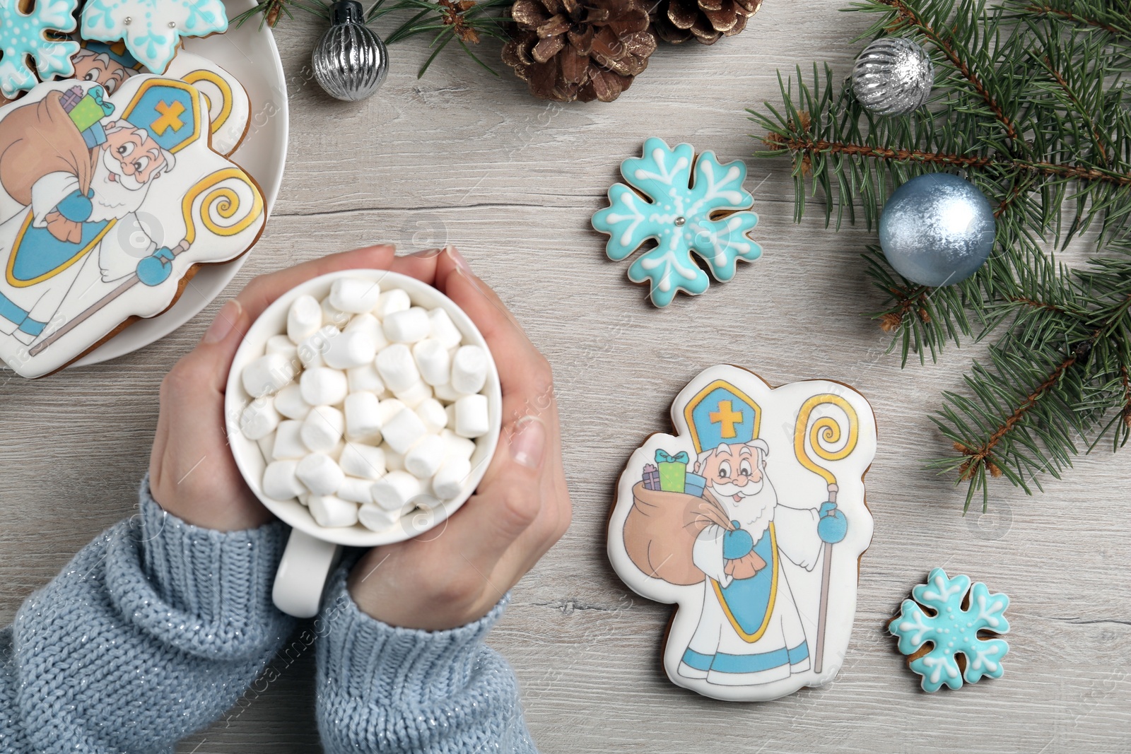 Photo of Woman holding cup of hot drink near tasty gingerbread cookies at wooden table, top view. St. Nicholas Day celebration