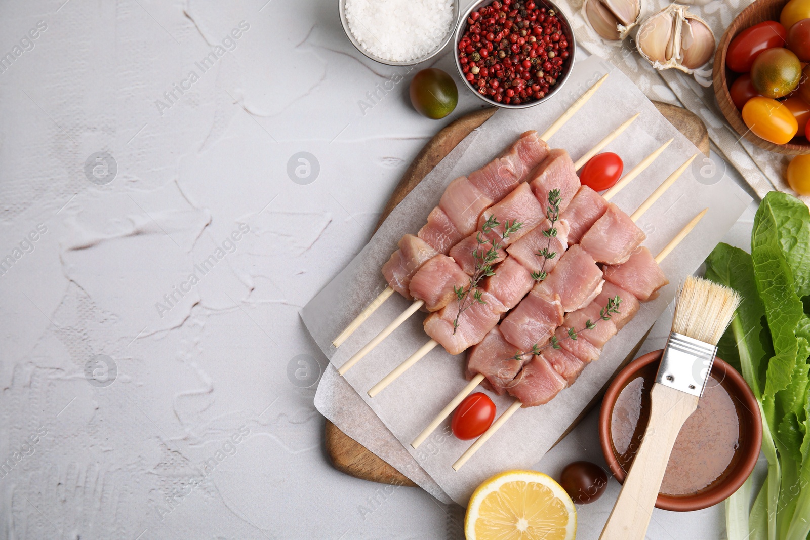 Photo of Flat lay composition of skewers with cut raw meat, thyme, tomatoes and marinade on light textured table. Space for text