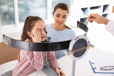 Photo of Little girl with mother visiting children's doctor in clinic. Eye examination