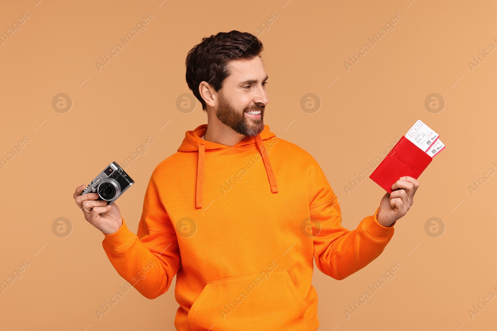 Photo of Smiling man with passport, camera and tickets on beige background