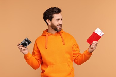 Smiling man with passport, camera and tickets on beige background