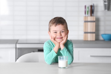 Cute little boy with glass of milk at table in kitchen