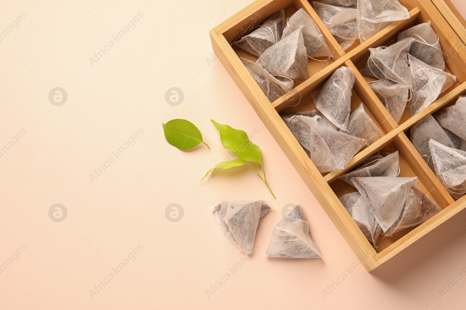 Photo of Many tea bags in wooden box and leaves on color background, flat lay. Space for text