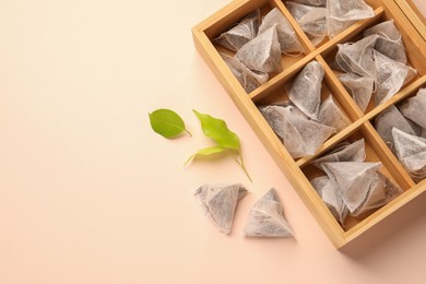 Photo of Many tea bags in wooden box and leaves on color background, flat lay. Space for text