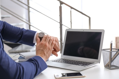 Young businessman checking time on his wristwatch at workplace. Time management