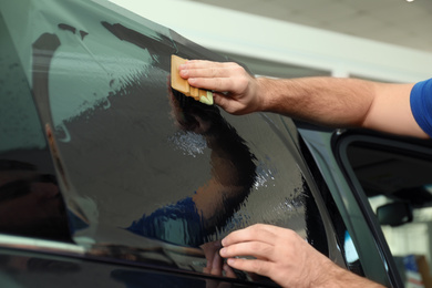 Worker tinting car window with foil in workshop, closeup