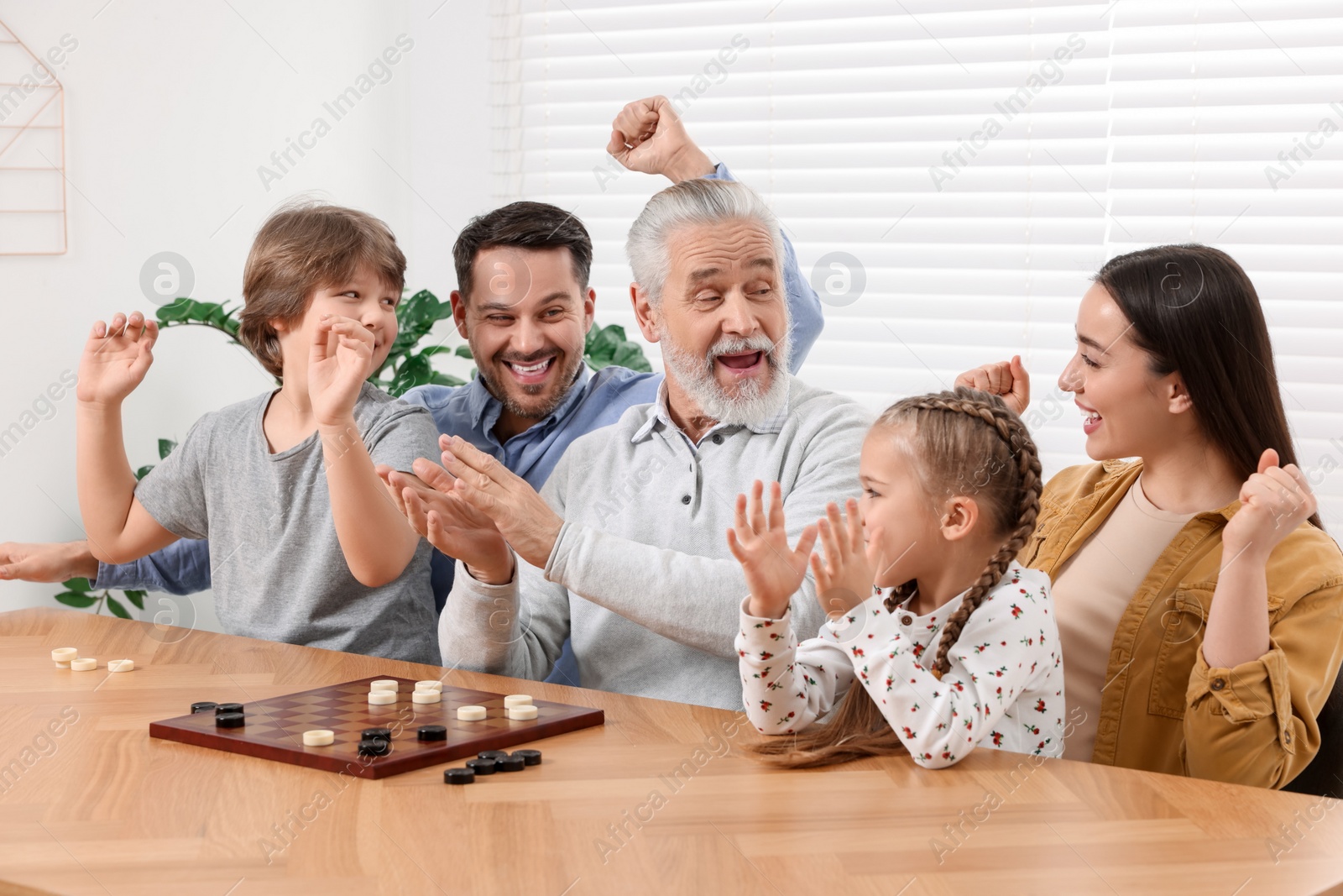 Photo of Emotional family playing checkers at wooden table in room