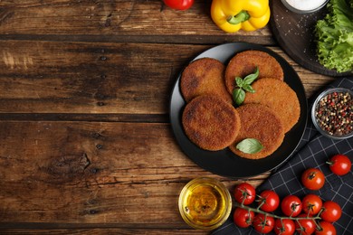 Photo of Delicious fried breaded cutlets, spices and vegetables on wooden table, flat lay. Space for text
