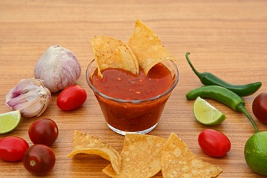 Photo of Tasty salsa sauce, nachos and different ingredients on wooden table