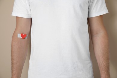 Photo of Blood donation concept. Man with adhesive plaster on arm against beige background, closeup