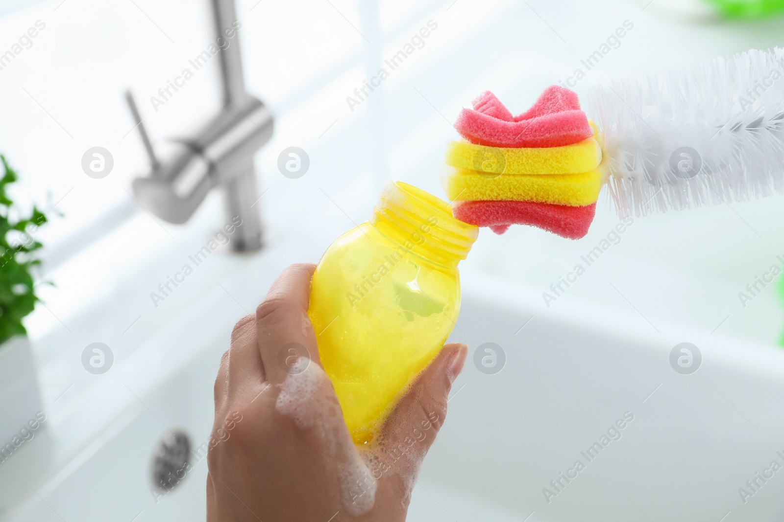 Photo of Woman washing baby bottle with brush in kitchen, closeup