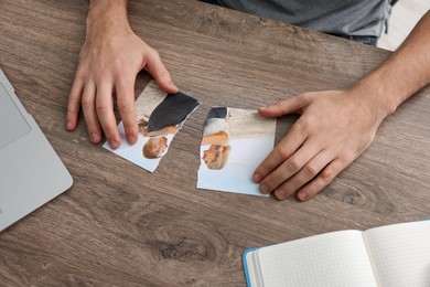 Photo of Man with parts of photo at table indoors, closeup. Divorce concept