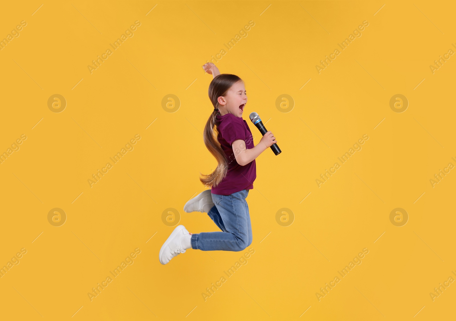 Photo of Cute little girl with microphone singing on yellow background