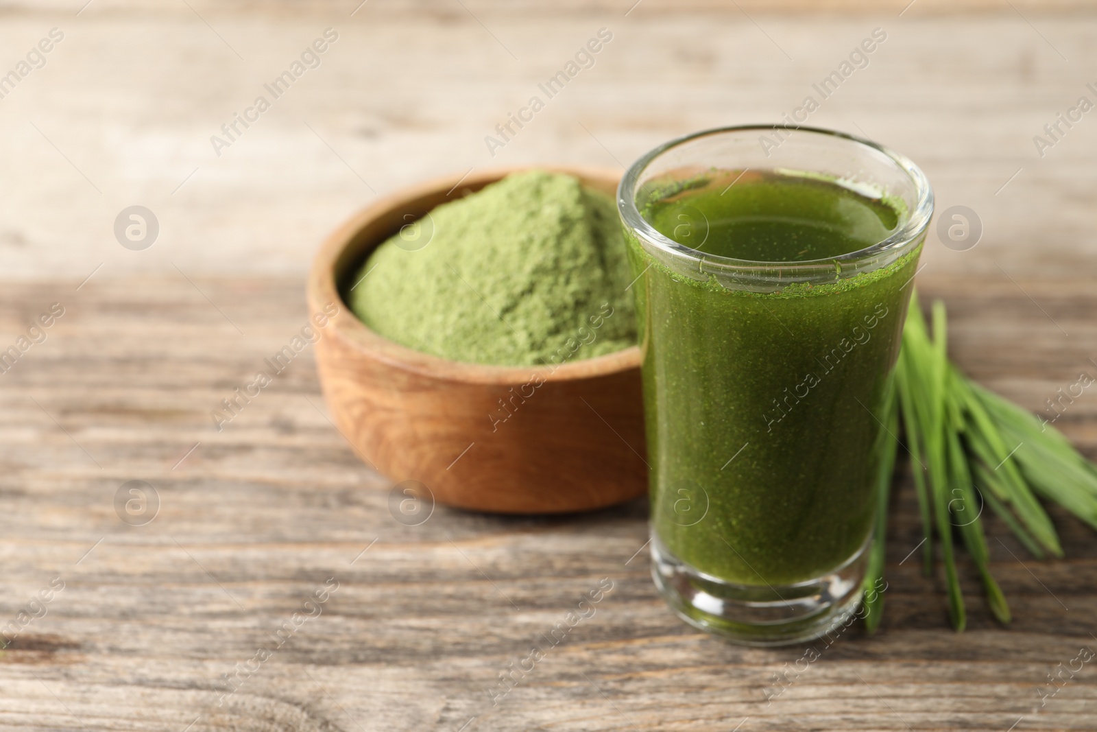 Photo of Wheat grass drink in shot glass on wooden table, closeup. Space for text