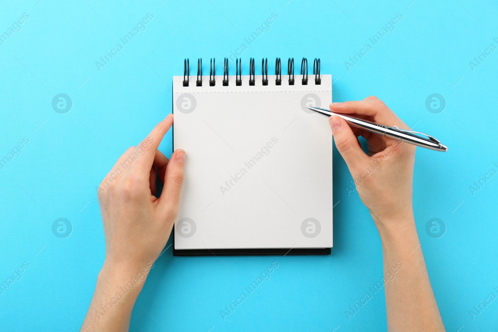 Photo of Woman writing in notebook on light blue background, top view