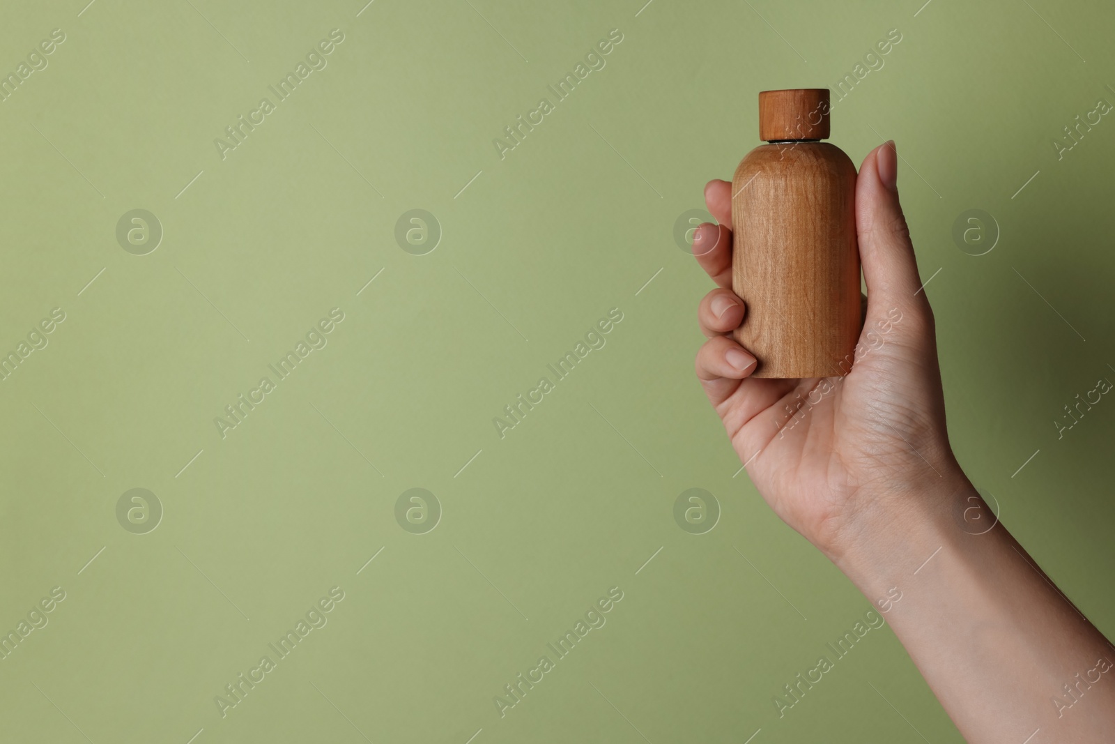 Photo of Woman holding bottle of cosmetic product on pale olive background, closeup. Space for text