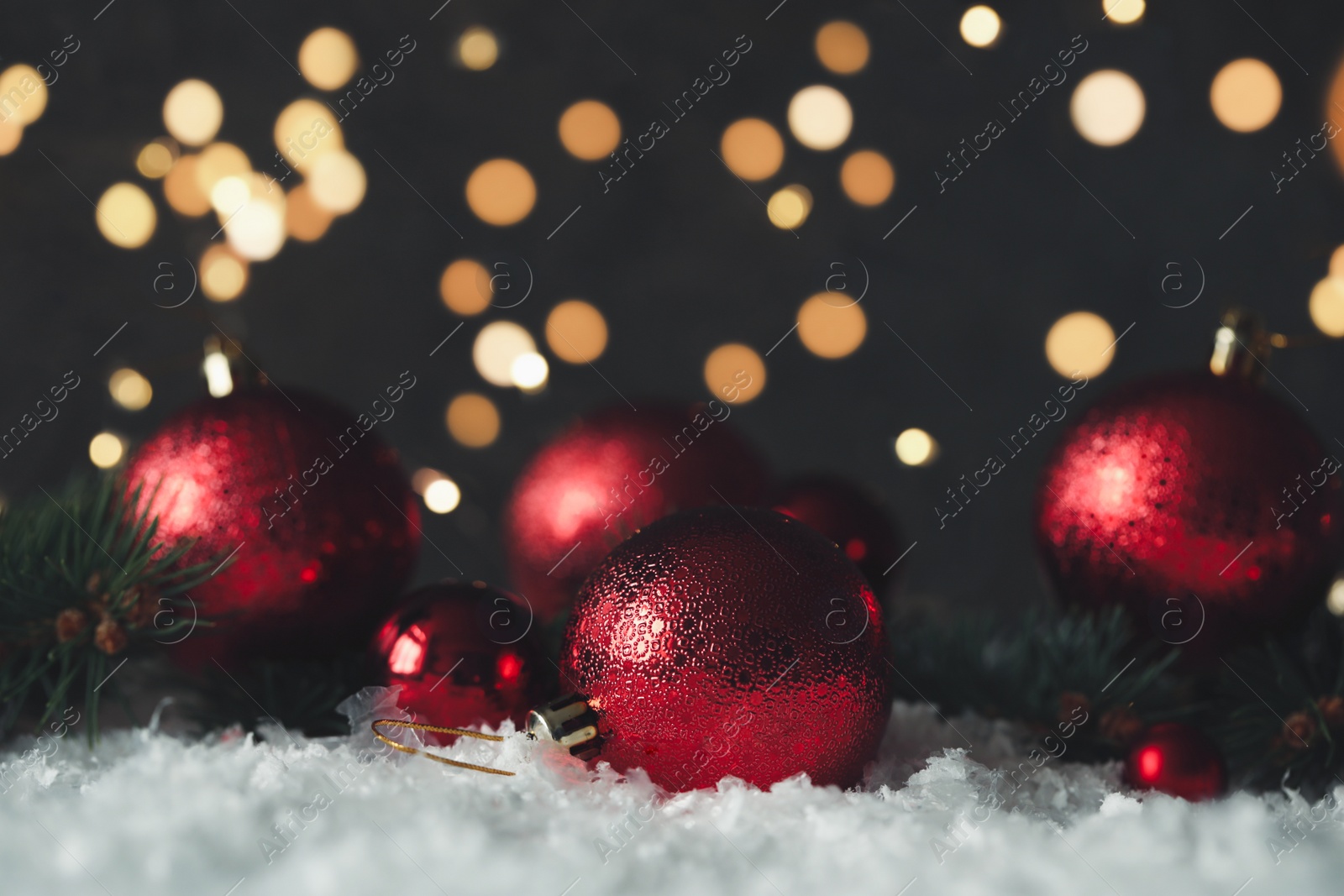 Photo of Beautiful Christmas balls and fir branches on snow against blurred festive lights. Space for text