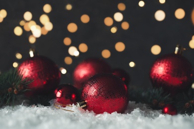 Beautiful Christmas balls and fir branches on snow against blurred festive lights. Space for text