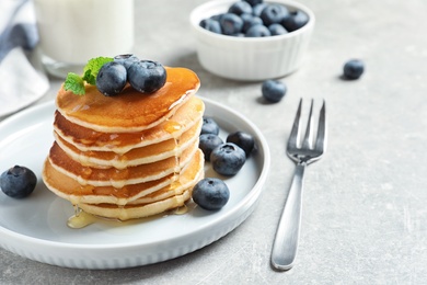 Photo of Plate of tasty pancakes with blueberries and honey on light grey table
