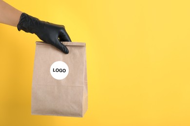 Woman holding paper bag with logo on yellow background, closeup. Space for text