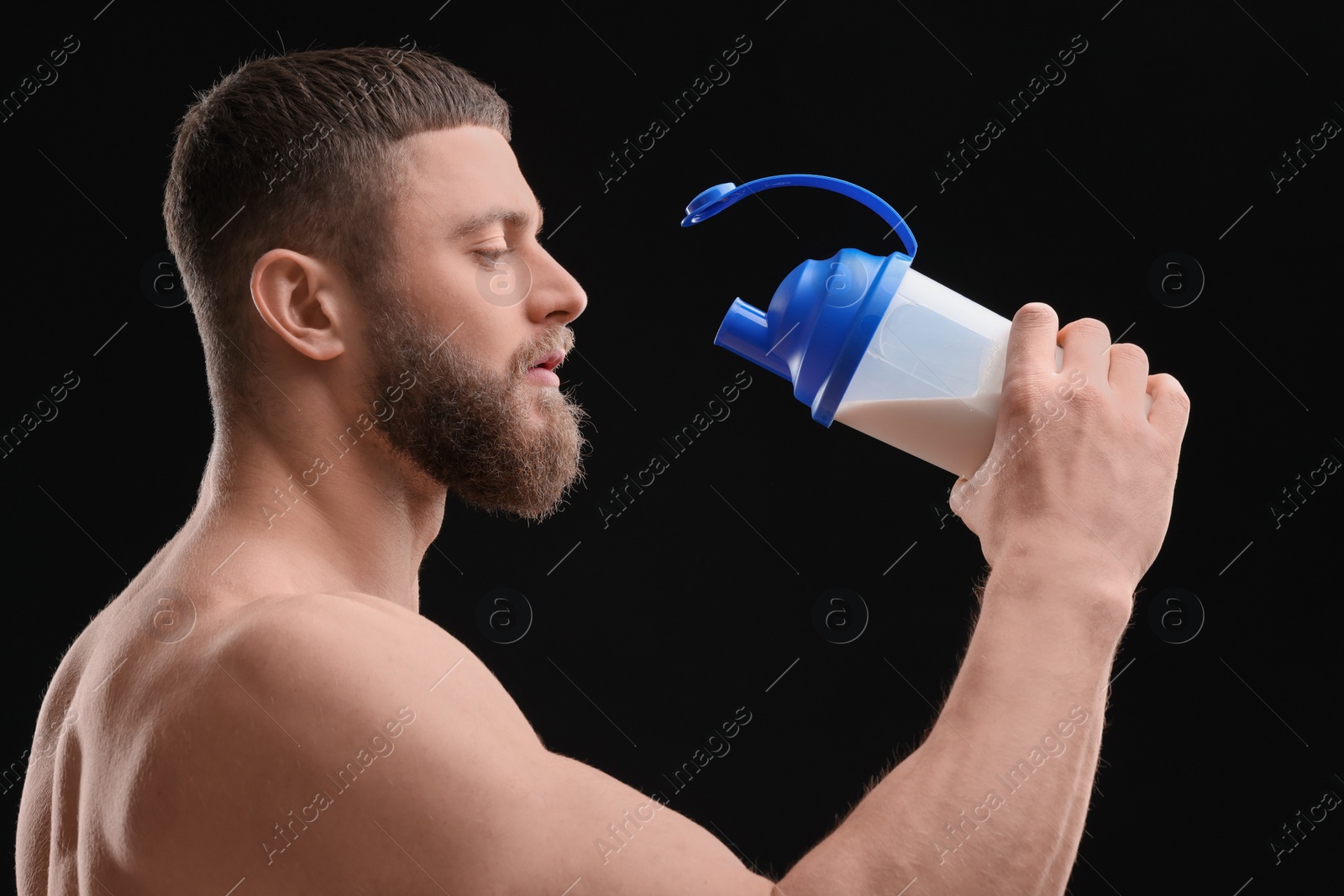 Photo of Young man with muscular body drinking protein shake on black background