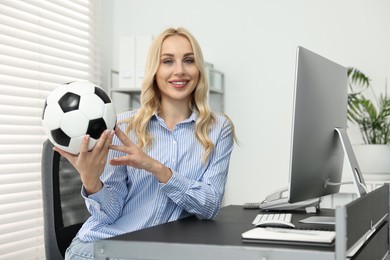 Happy woman with soccer ball at table in office