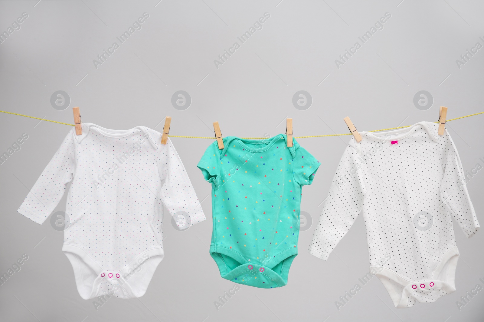 Photo of Baby clothes hanging on washing line against gray background