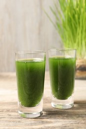 Photo of Wheat grass drink in shot glasses on wooden table, closeup