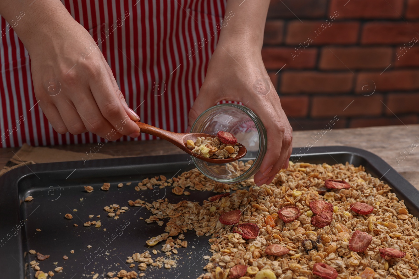 Photo of Woman putting granola from baking tray into jar at table, closeup