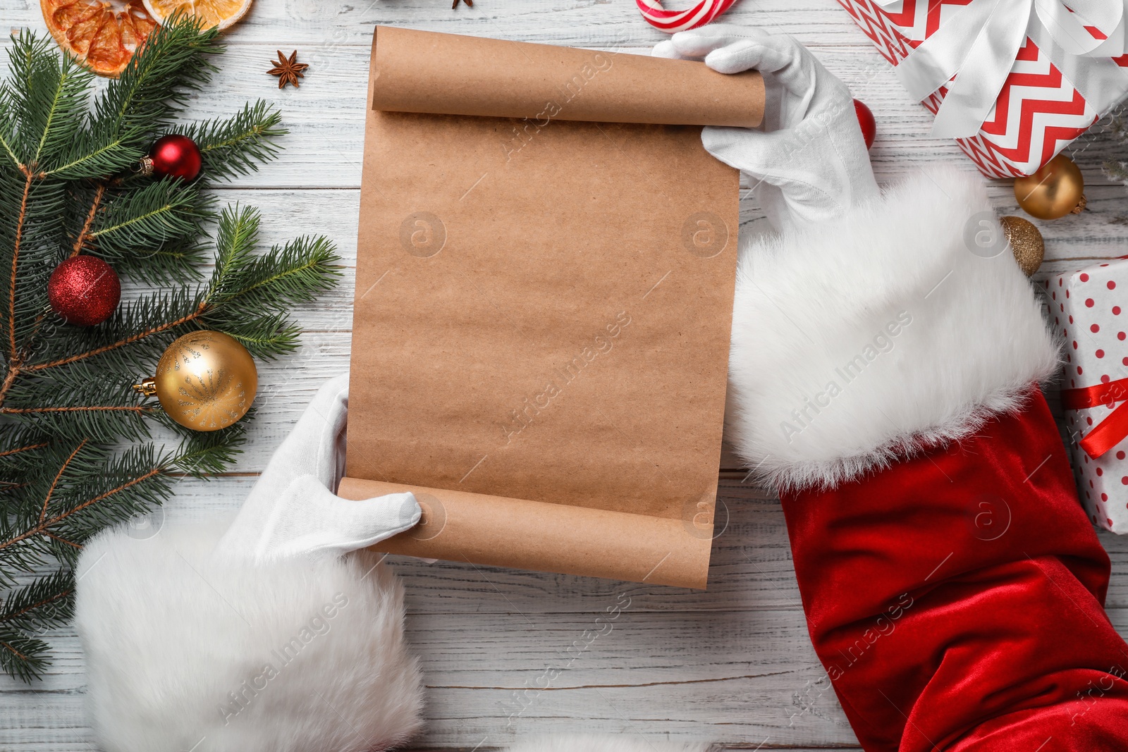 Photo of Santa Claus holding scroll and Christmas decor on wooden background, top view