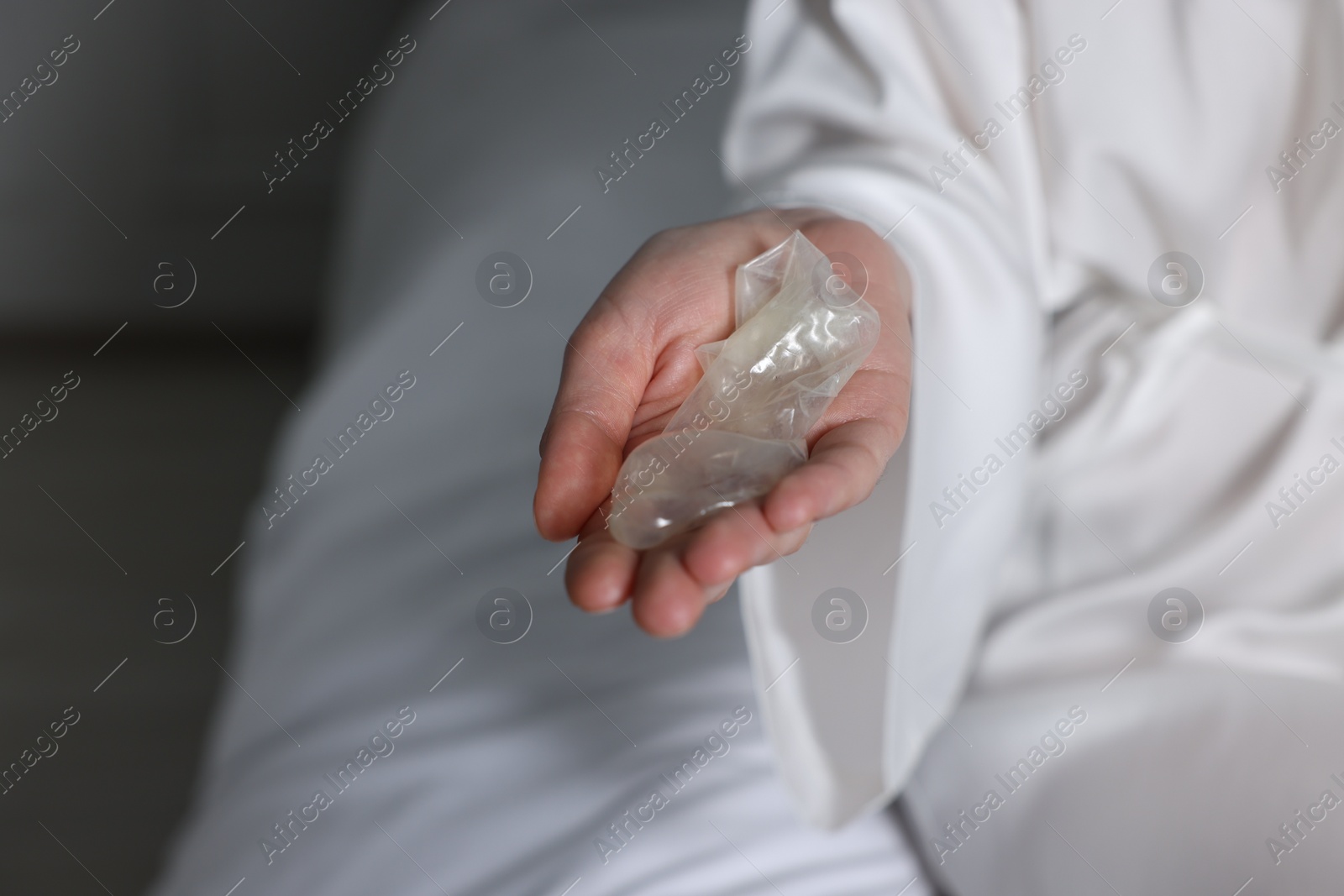 Photo of Woman holding unrolled condom in bedroom, closeup. Safe sex