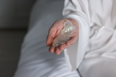 Woman holding unrolled condom in bedroom, closeup. Safe sex