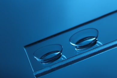 Pair of contact lenses on glass against blue background, closeup
