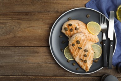 Photo of Delicious chicken fillets with capers and lemon served on wooden table, flat lay. Space for text