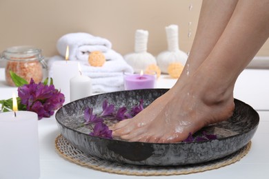 Photo of Woman pouring water onto her feet in bowl on white floor, closeup. Spa treatment