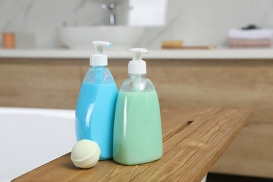 Photo of Wooden tray with bottles of shower gels and bath bomb on tub indoors, space for text