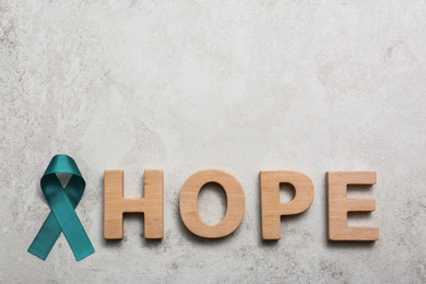 Photo of Word Hope made of wooden letters and teal awareness ribbon on grey background. Symbol of social and medical issues