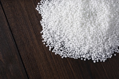 Photo of Pellets of ammonium nitrate on wooden table, flat lay with space for text. Mineral fertilizer