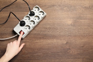 Photo of Woman pressing button of power strip on wooden floor, top view. Space for text
