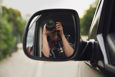 Photo of Private detective with camera spying from auto, view through car side mirror