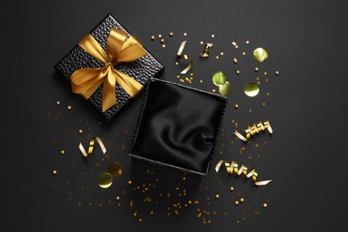 Open gift box, confetti and streamers on black  background, flat lay