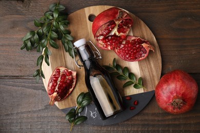 Photo of Tasty pomegranate sauce in bottle, fruits and branches on wooden table, flat lay