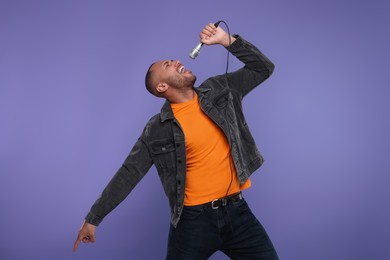 Photo of Handsome man with microphone singing on violet background